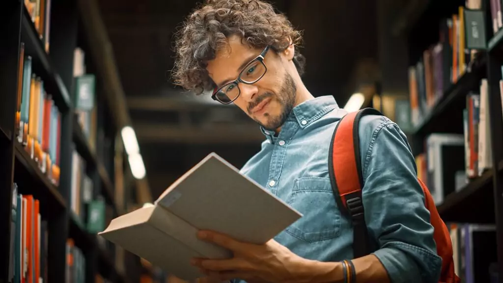 rapaz lendo livro em biblioteca