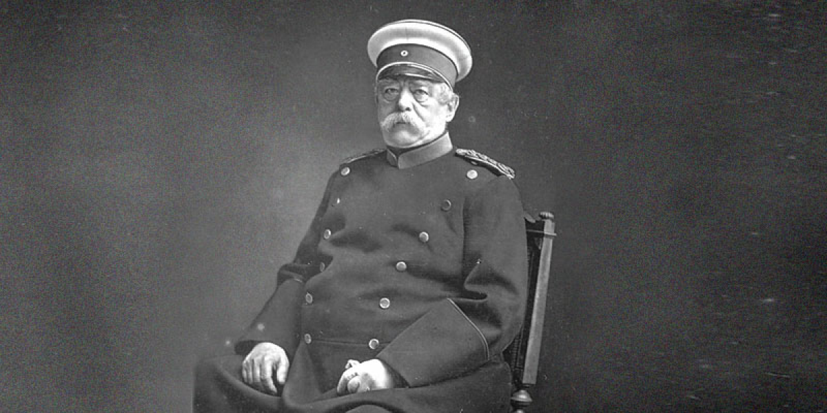 Retrato de Otto von Bismark sentado. Bismark é um homem idoso e usa um bigode volumoso branco. Ele está usando um chapéu militar. Estado de bem-estar social. 