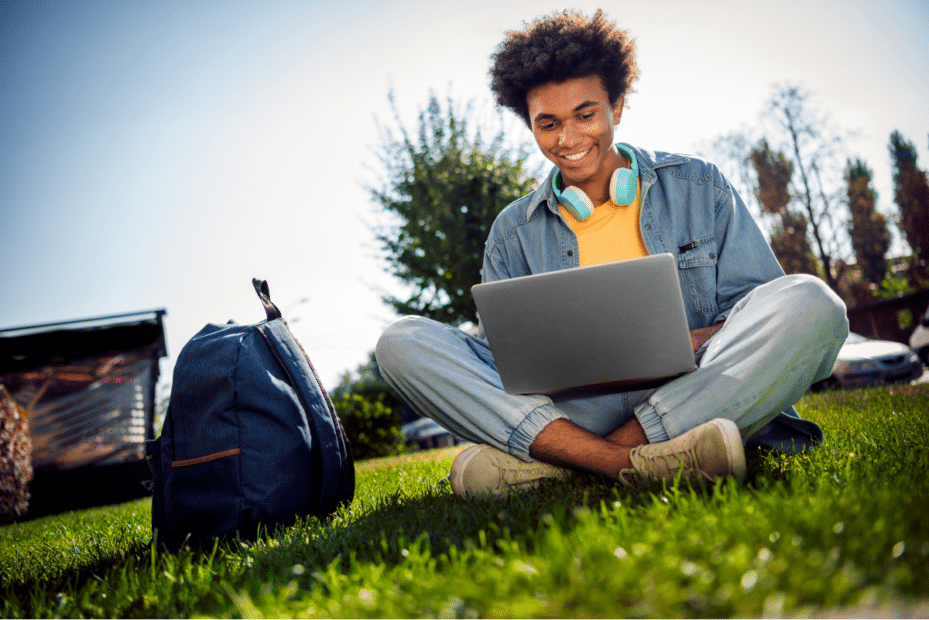 Jovem homem estudando com o computador em um parque. Ferias de verao.