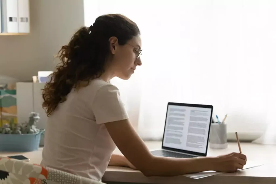 mulher concentrada escrevendo com texto aberto no computador