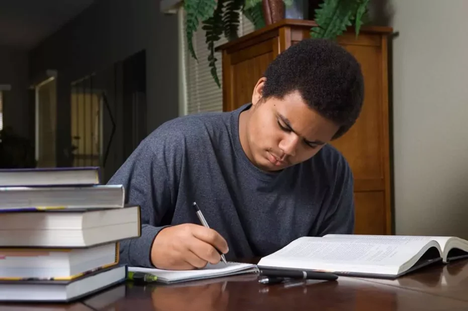 rapaz escrevendo em caderno com livros ao seu redor