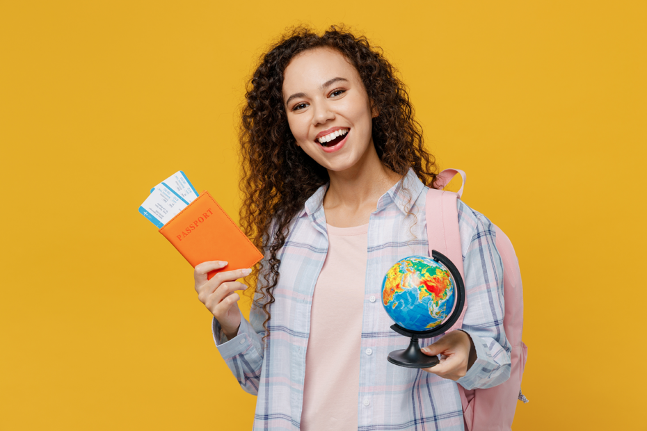 Mulher sorri segurando seu passaporte e um globo terrestre. Como entrar na faculdade.